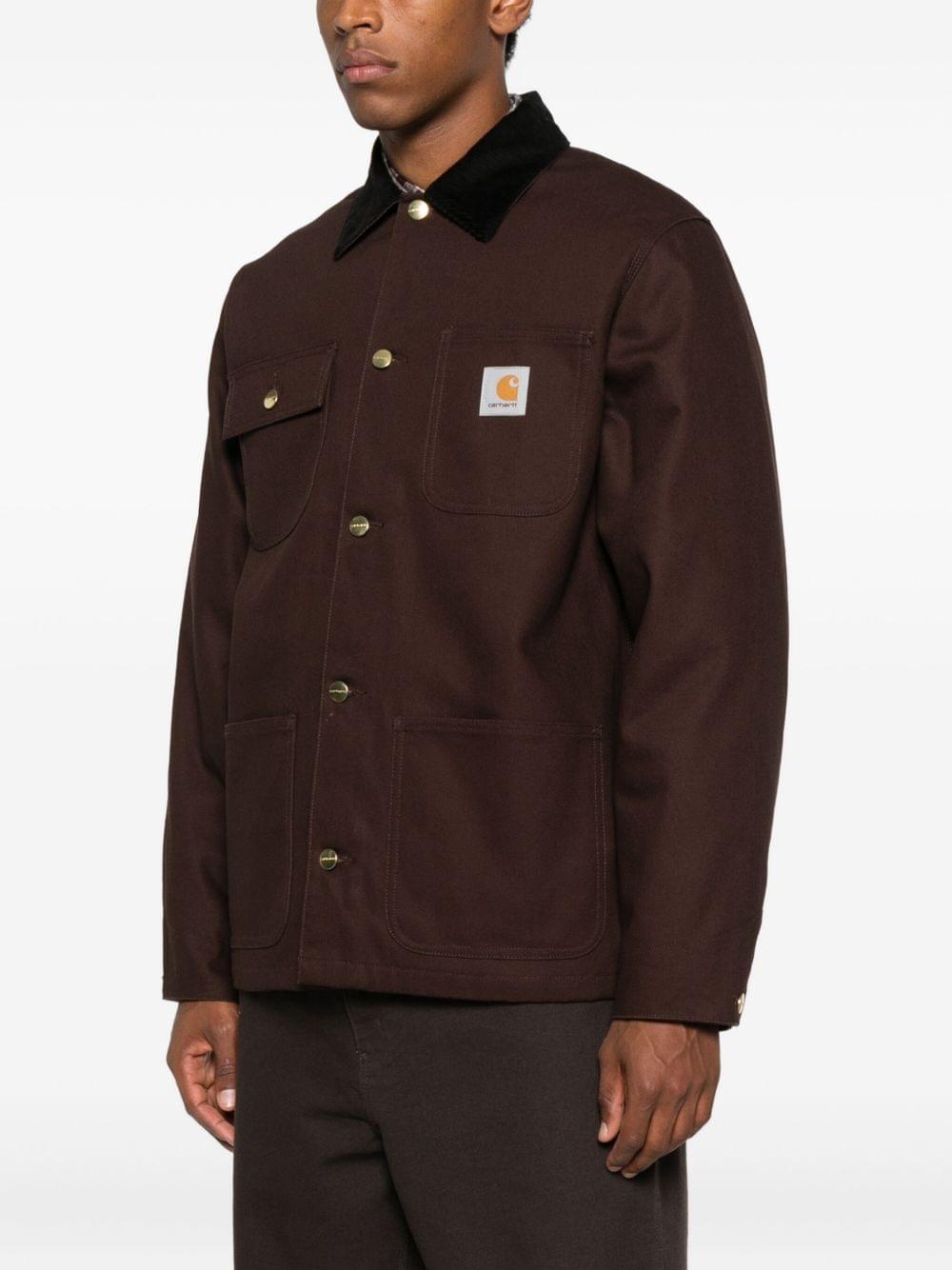 Carhartt Wip Main jacket in dark color with front pockets, casual style, made of durable fabric, displayed on a hanger.