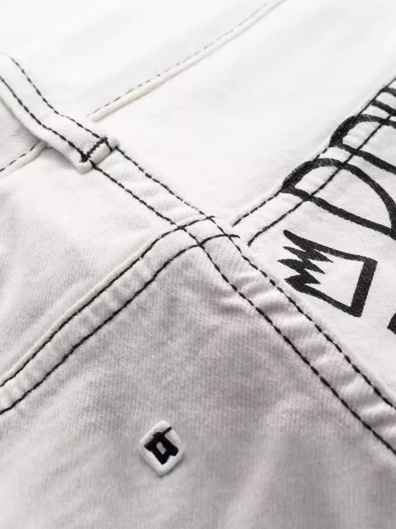 White Luxenk© "Graffiti Slim" jeans by Trendsi, showcasing a slim fit design with detailed graffiti-inspired stitching.